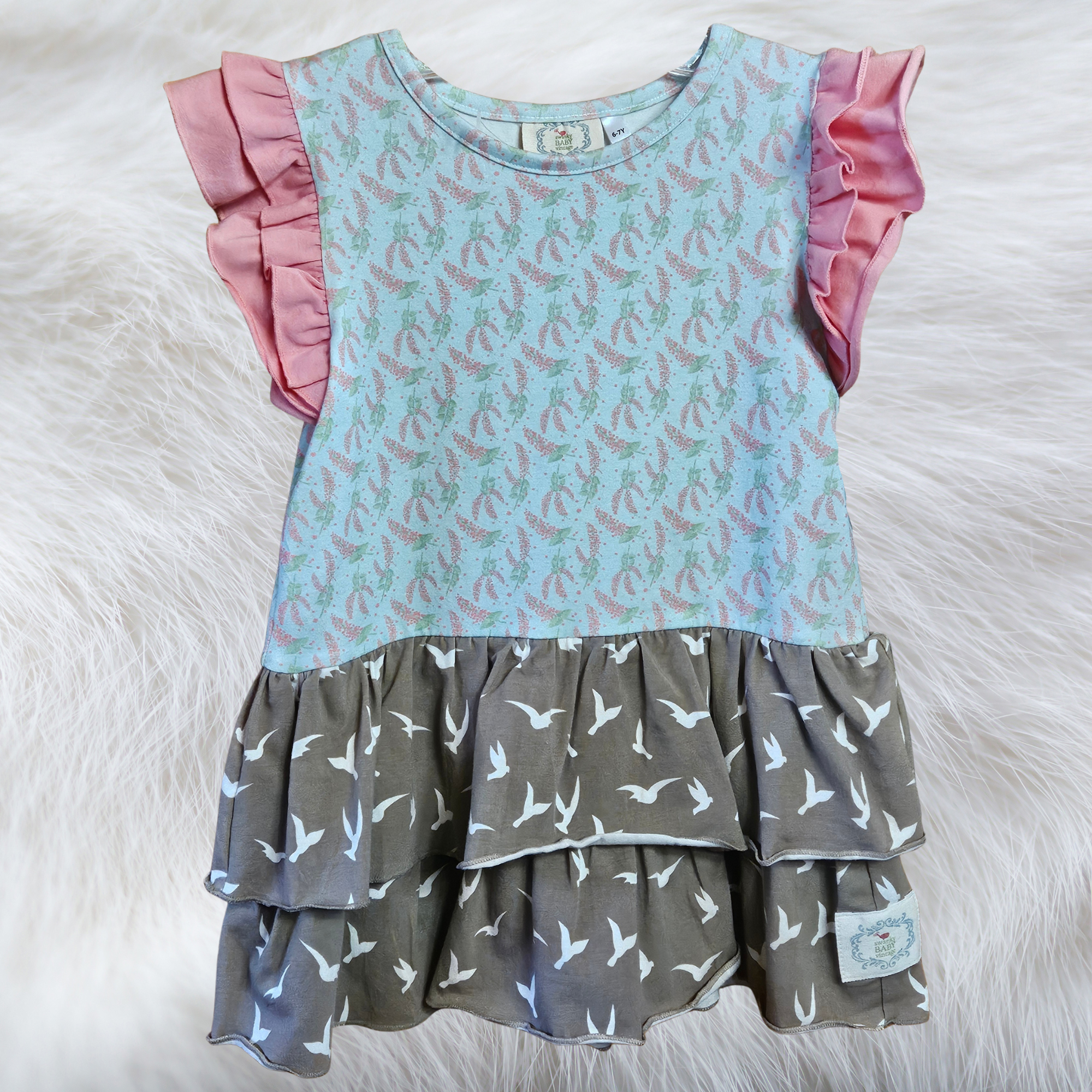 Two-tiered dress with pink ruffled sleeves and patterned layers on a white fur background