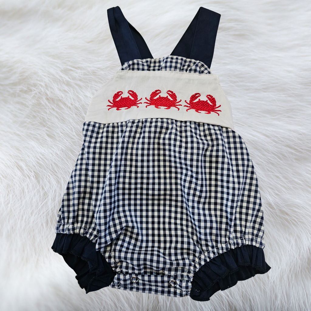 Black and white checkered romper with red crab design on a fluffy white surface