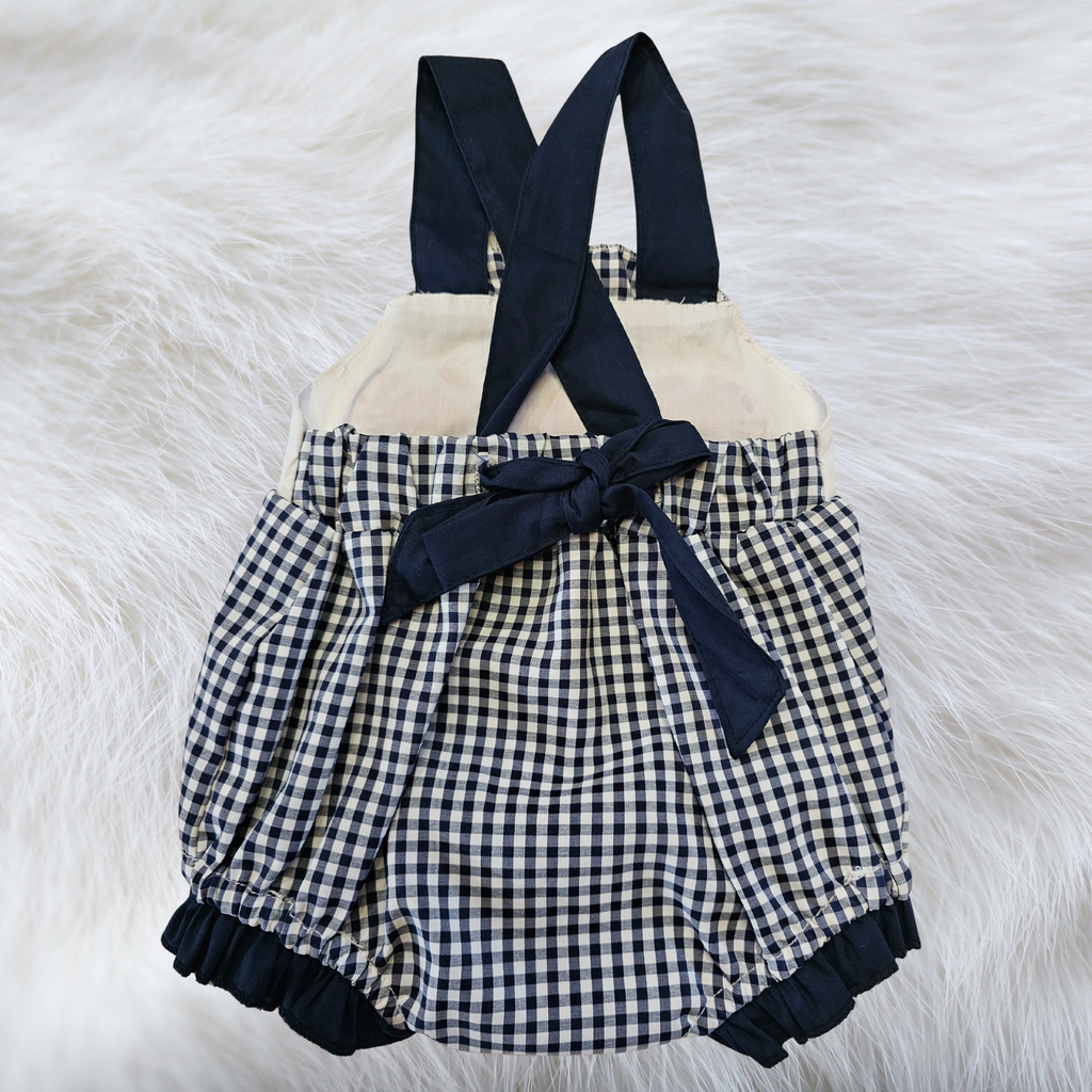 Checkered romper with navy straps on a fluffy white surface