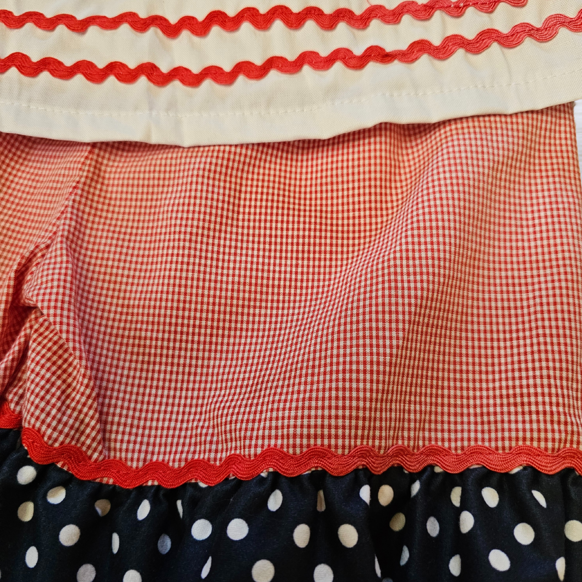 Close-up of a fabric with red checkered, red scalloped, and black polka dot patterns.