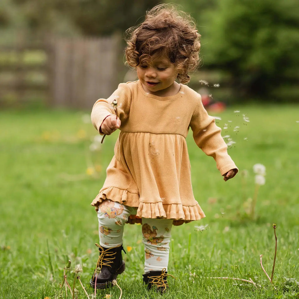Child in a yellow dress standing in a grassy field with dandelions.