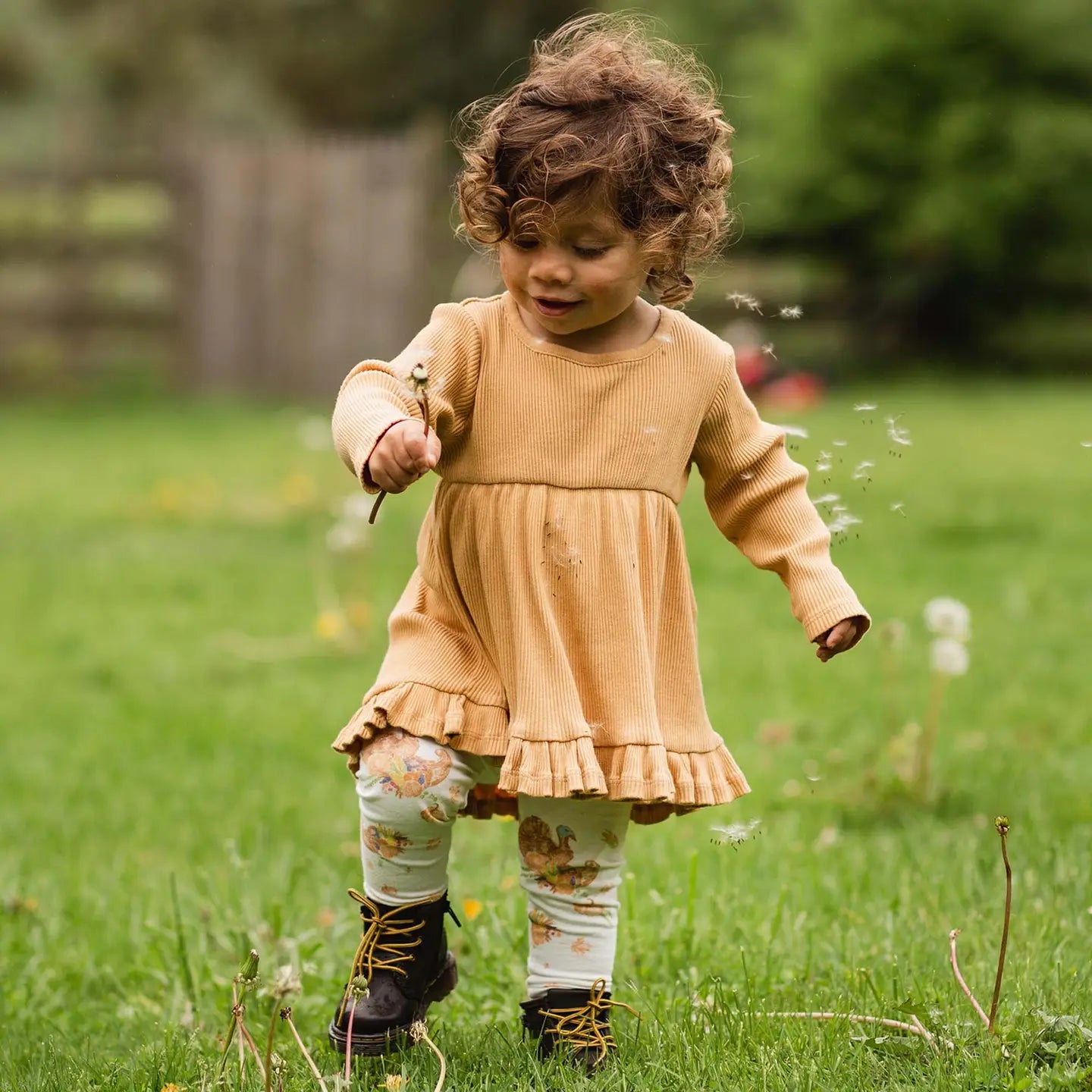 Child in a yellow dress standing in a grassy field with dandelions.