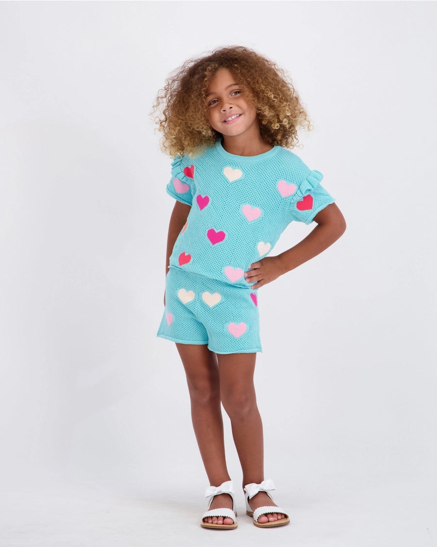 Child wearing a turquoise outfit with heart patterns on a white background