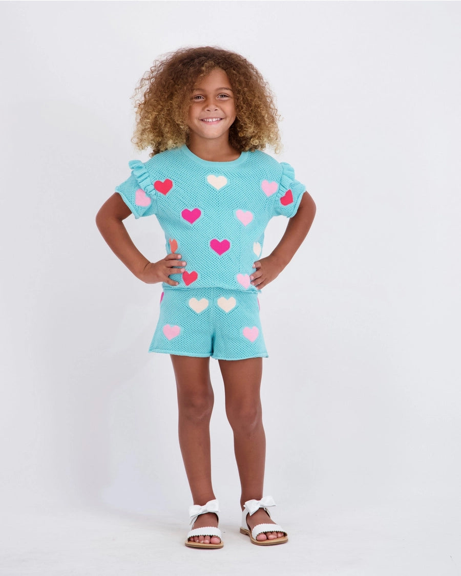Child wearing a turquoise outfit with heart patterns on a white background