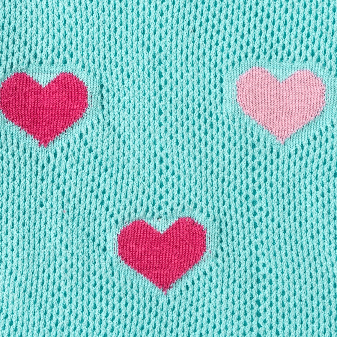 Close-up of a textured turquoise fabric with pink heart shapes.