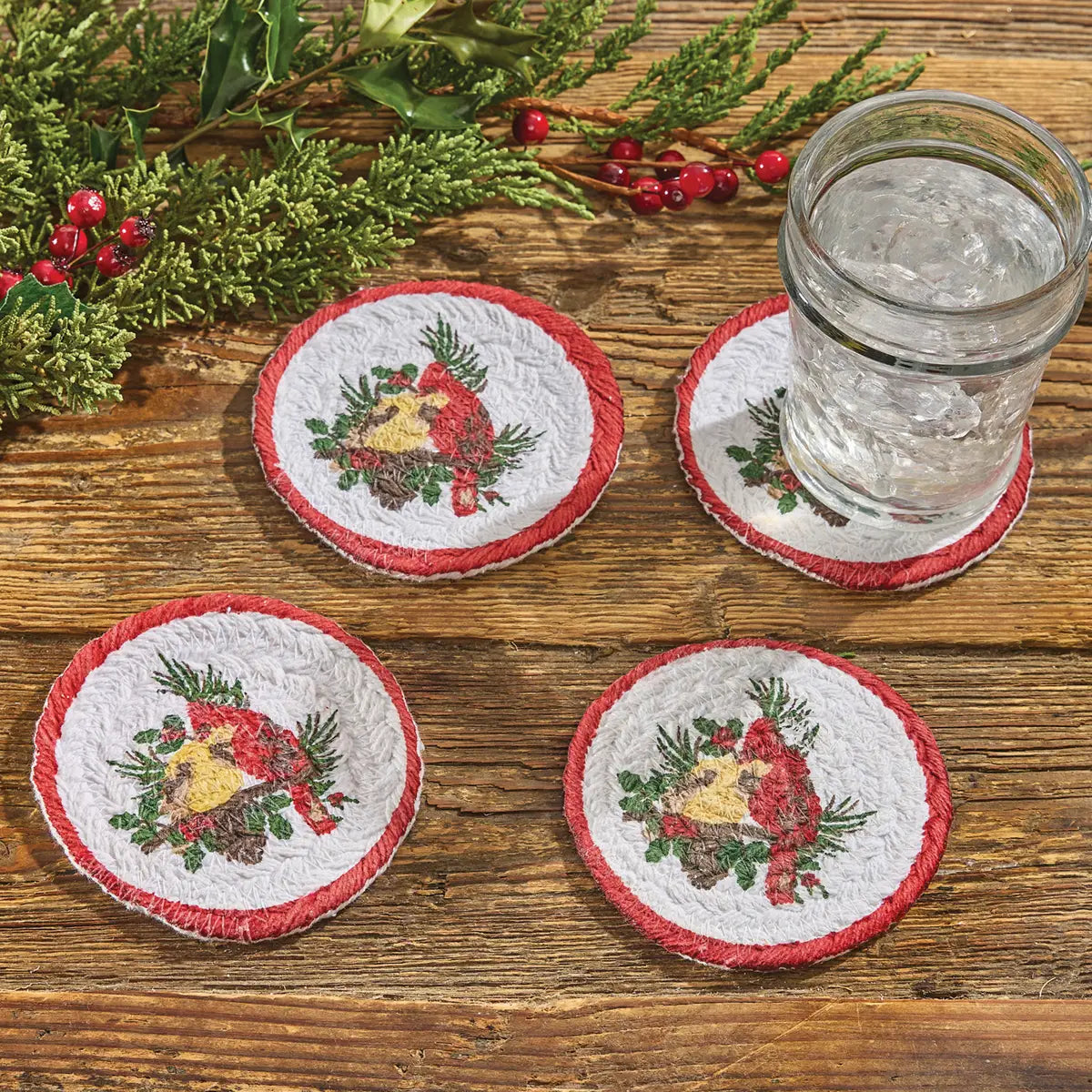 Set of four Christmas-themed coasters on a wooden surface with a glass of water.