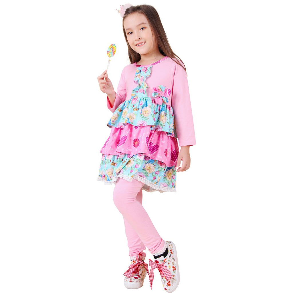 Young girl in a pink and floral outfit holding a lollipop on a white background