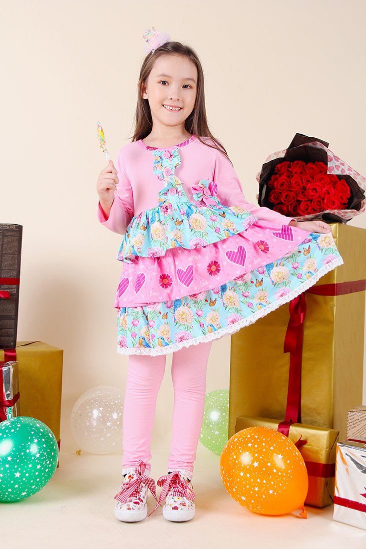 Young girl in a colorful dress holding flowers and a lollipop, surrounded by gift boxes and balloons.
