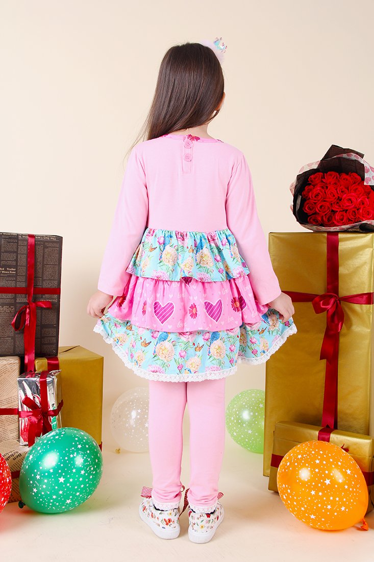 Child in a pink outfit with floral skirt standing among colorful gifts and balloons.