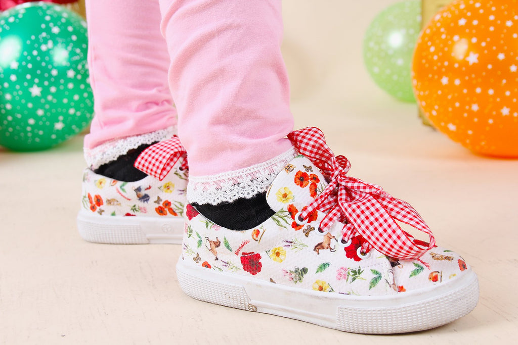Children's floral shoes with bows worn by a child, with colorful balloons in the background.