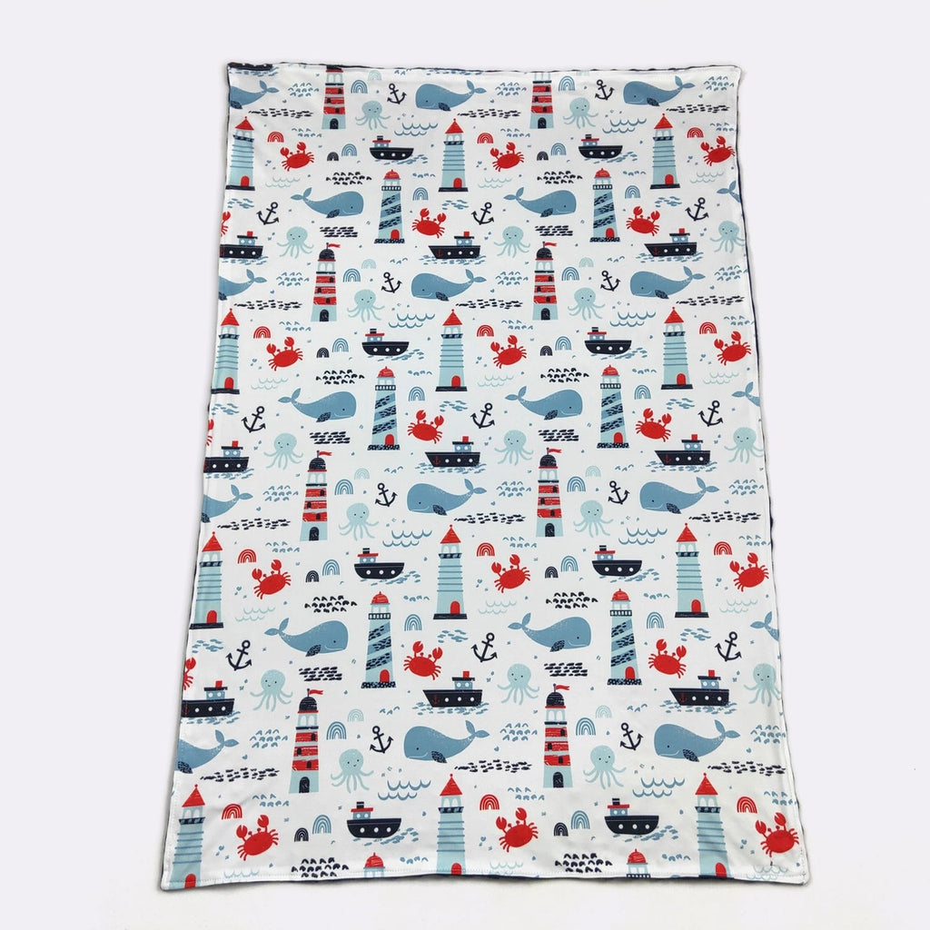 Fabric with nautical pattern featuring whales, lighthouses, and ships on a white background