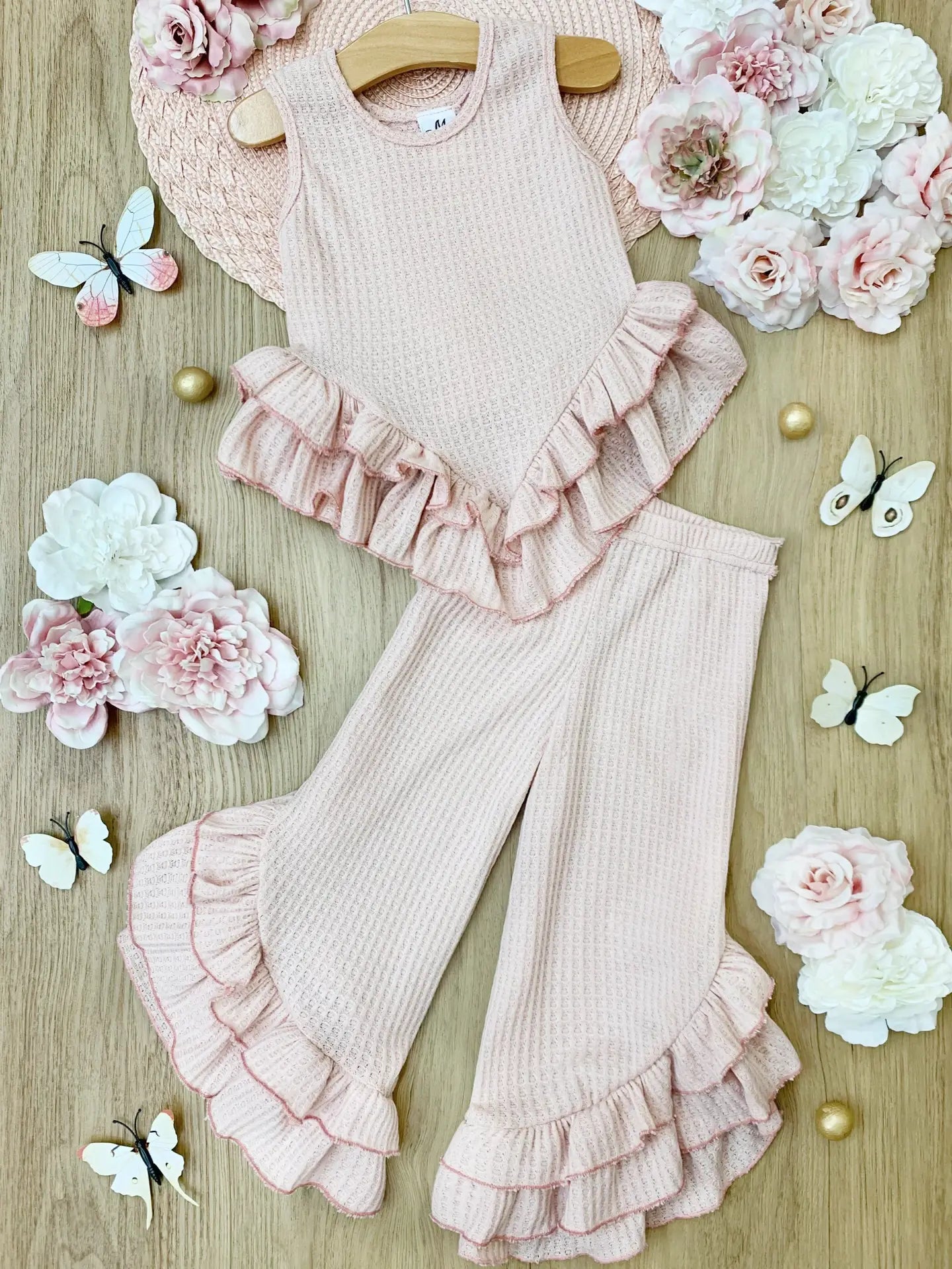 Pink baby outfit with ruffled details on a wooden surface with flowers and butterflies.