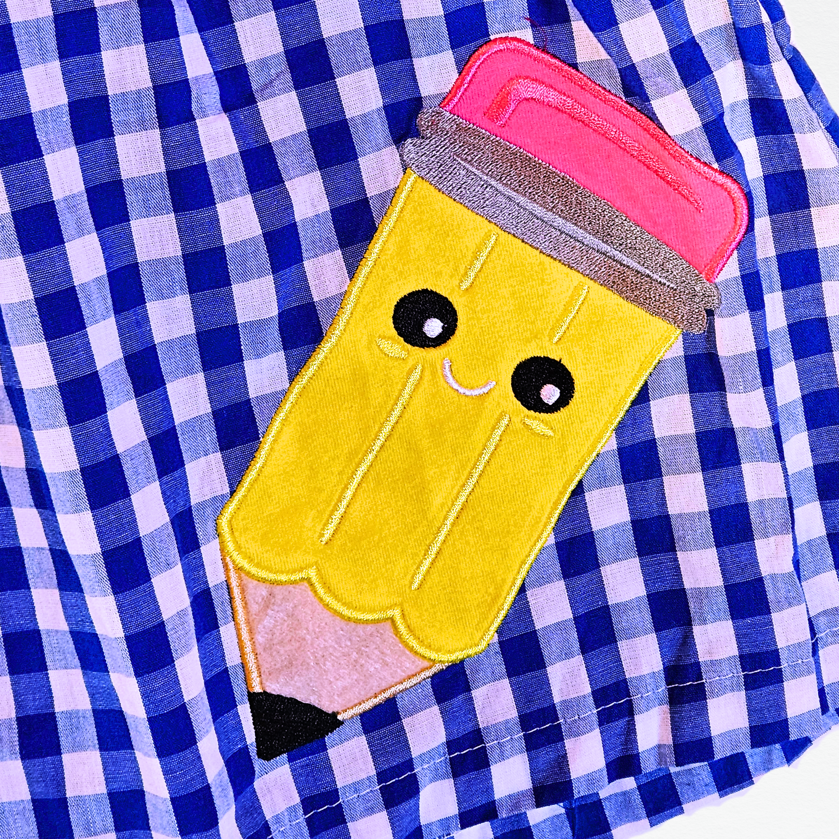 Embroidered yellow pencil with pink eraser on a blue checkered fabric background