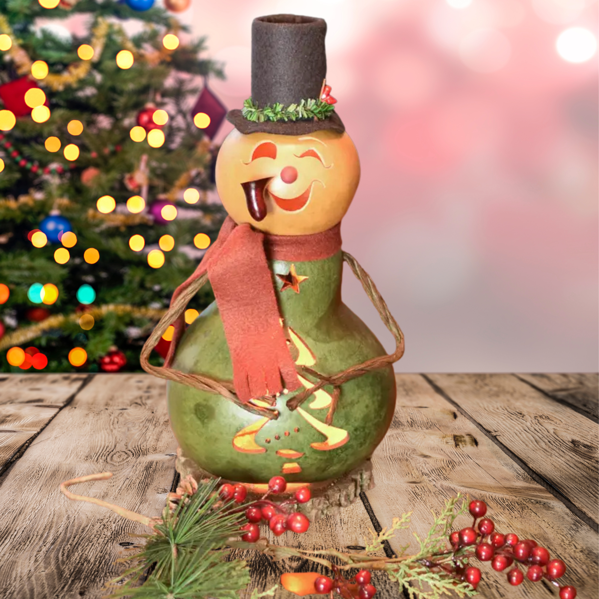 Decorative snowman gourd with a holly berry top hat and red felt scarf in front of a Christmas tree.
