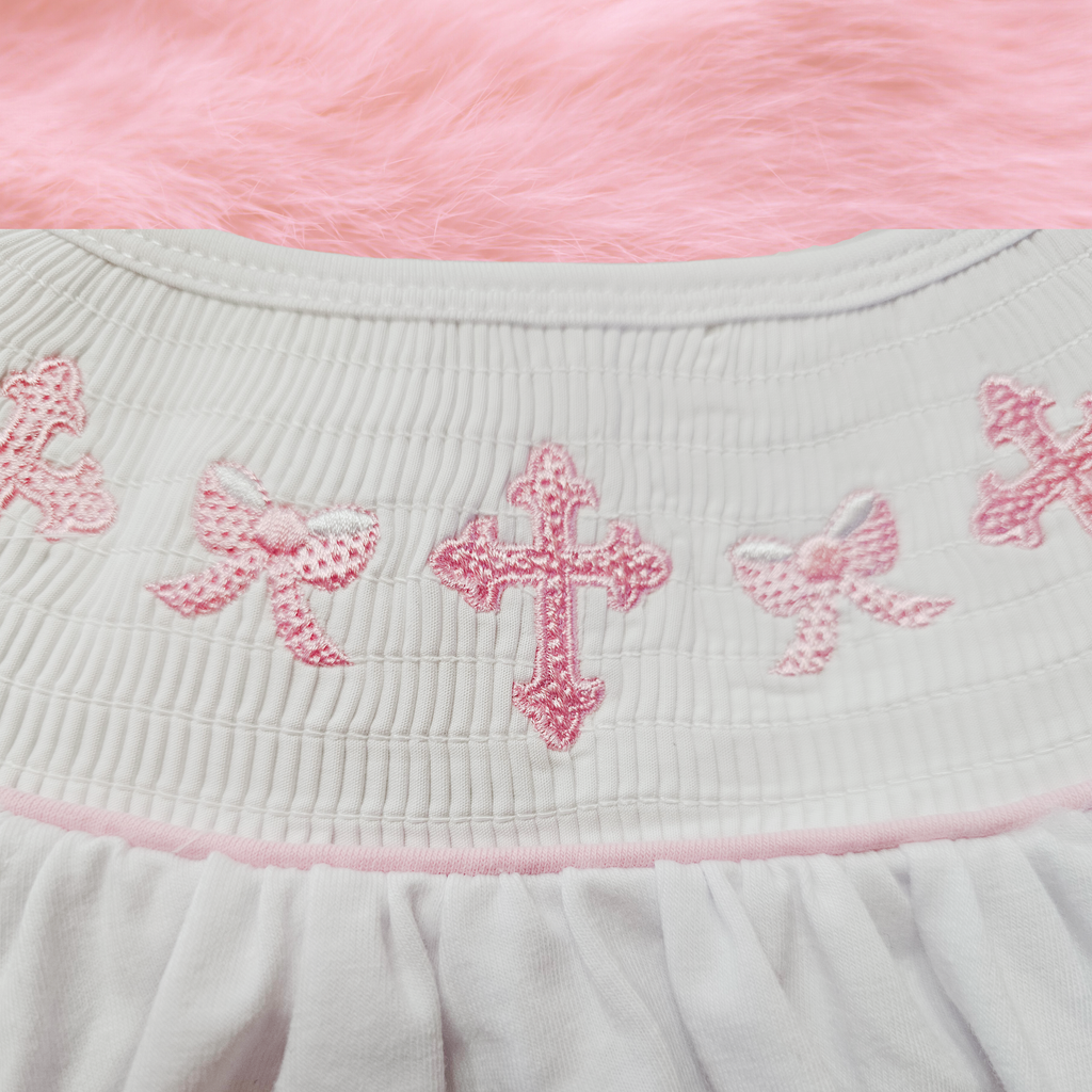 Close-up of a white fabric with pink embroidered crosses and bows on a pink background.