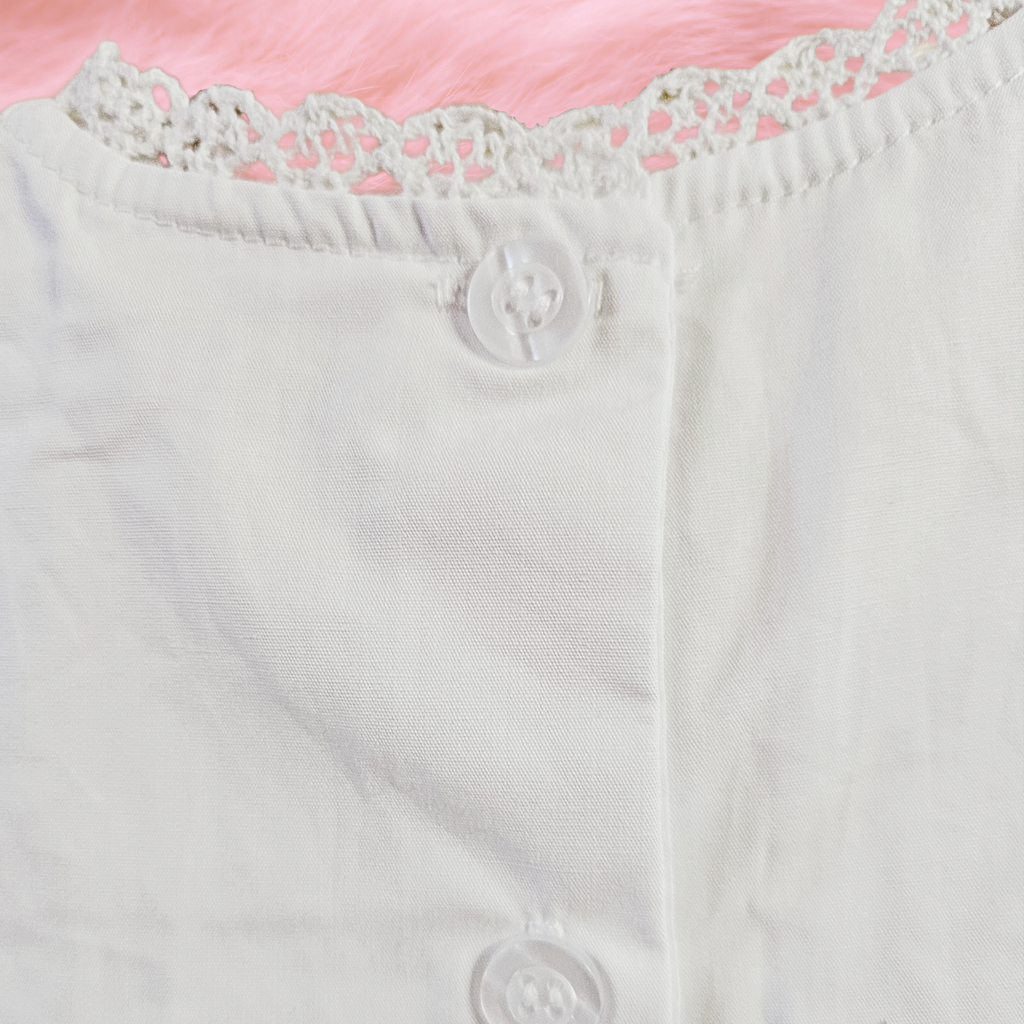 Close-up of a white garment with lace trim and buttons on a pink background