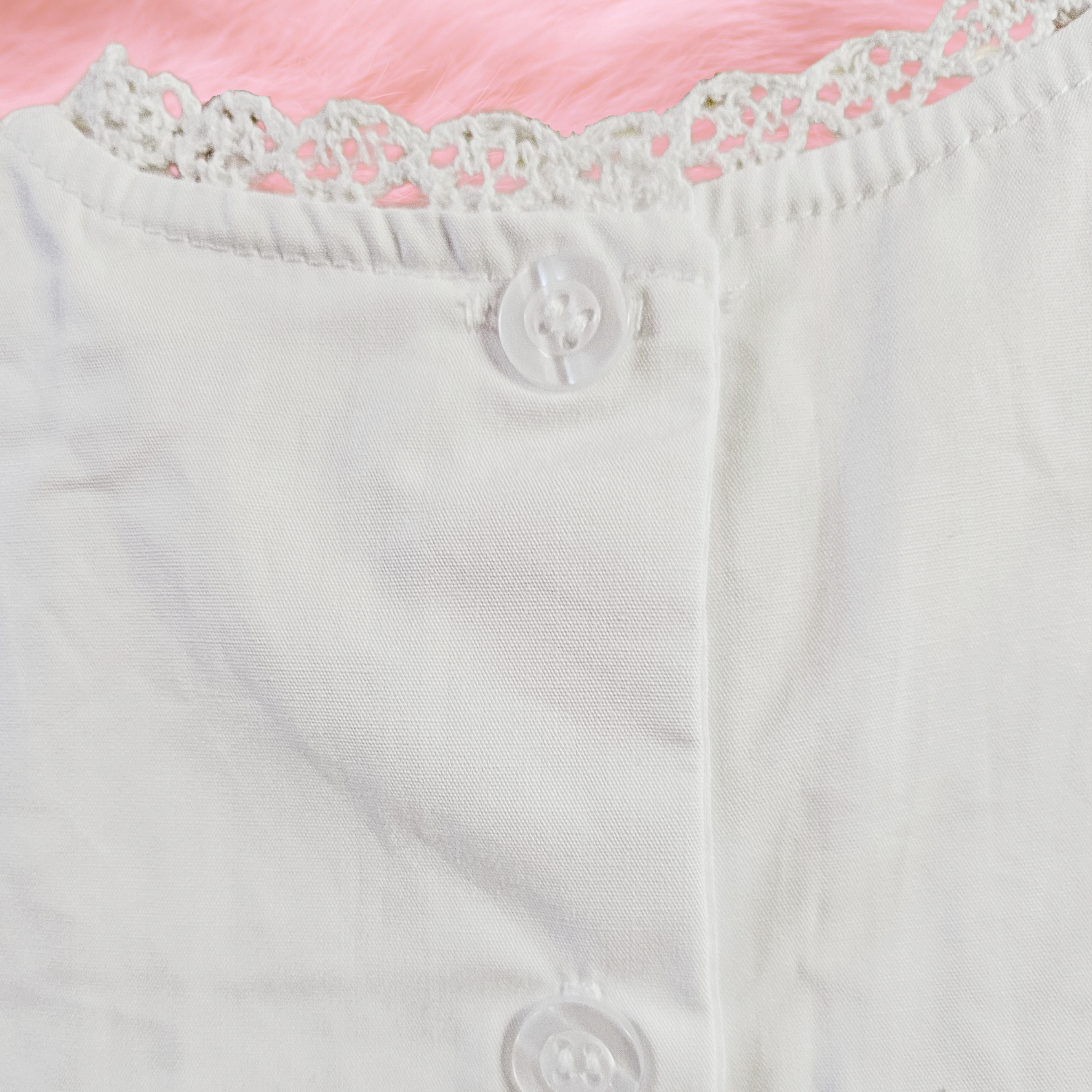 Close-up of a white garment with lace trim and buttons on a pink background