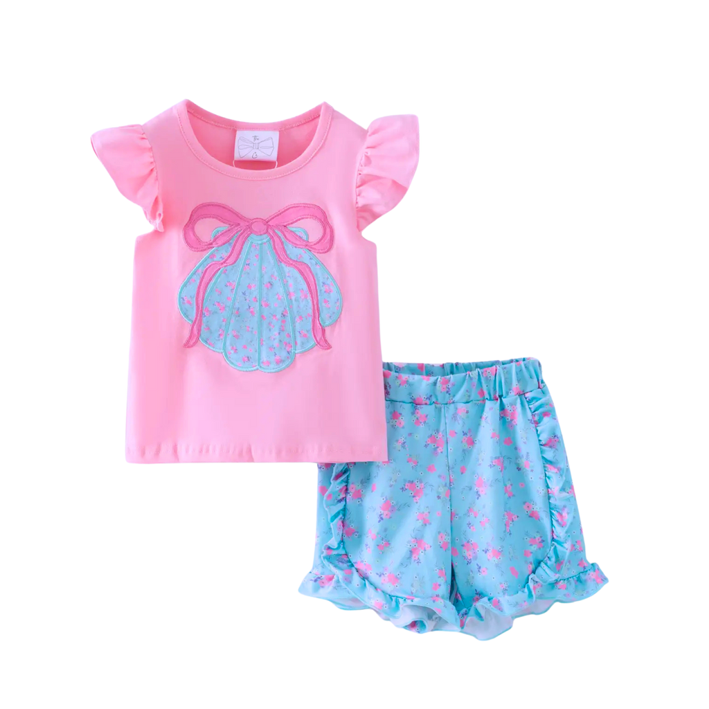 Pink top with seashell bow design and blue shorts with pink flowers on a white background