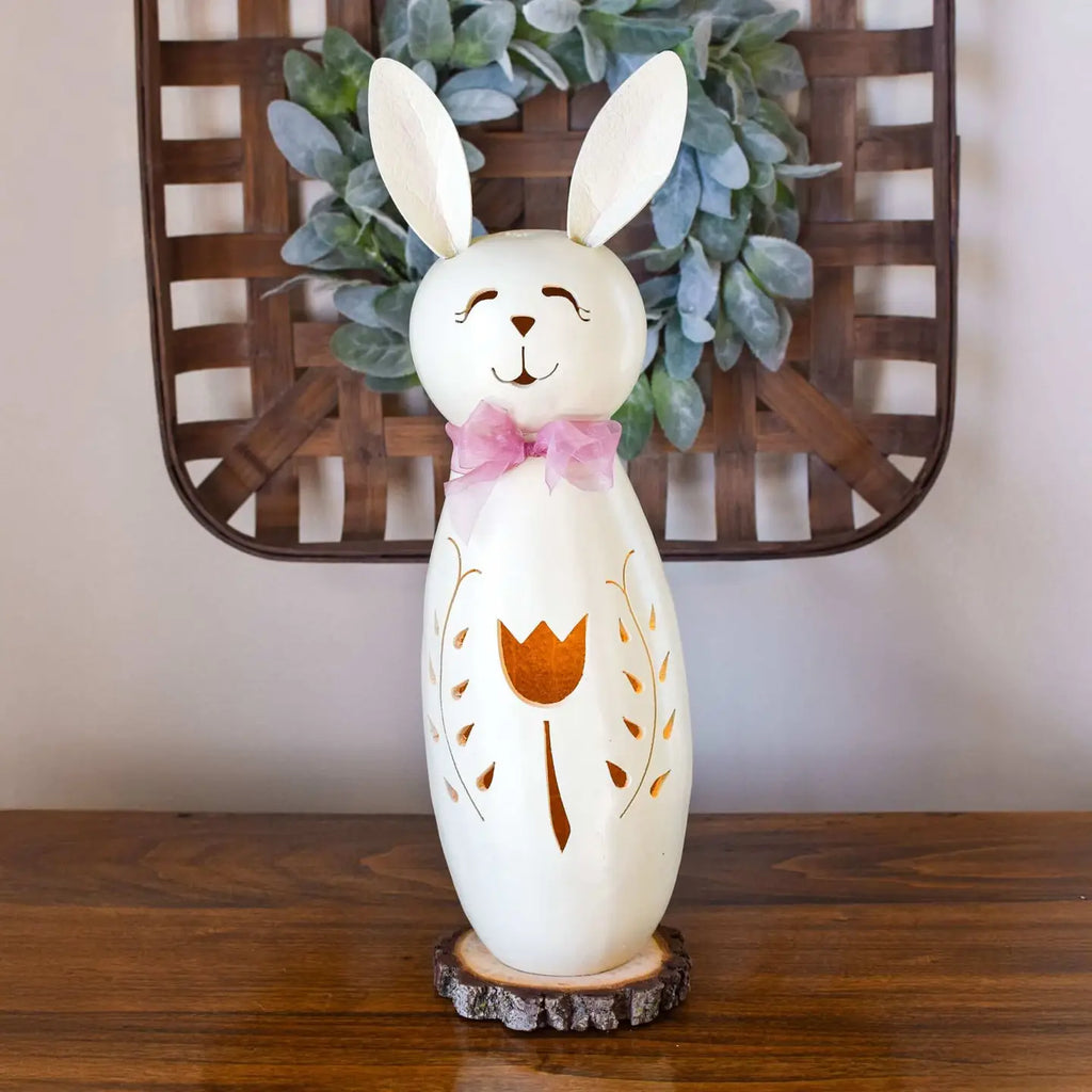 Decorative rabbit-shaped lamp with a bow tie on a wooden surface, with a wreath in the background.