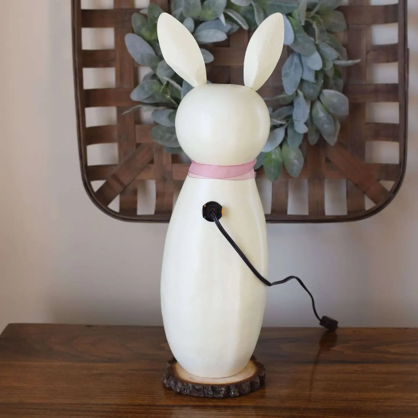 White rabbit-shaped lamp on a wooden surface with a decorative wreath in the background.