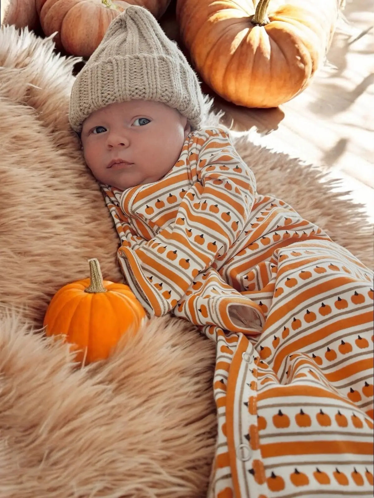 Baby in a patterned outfit with pumpkins on a fluffy surface