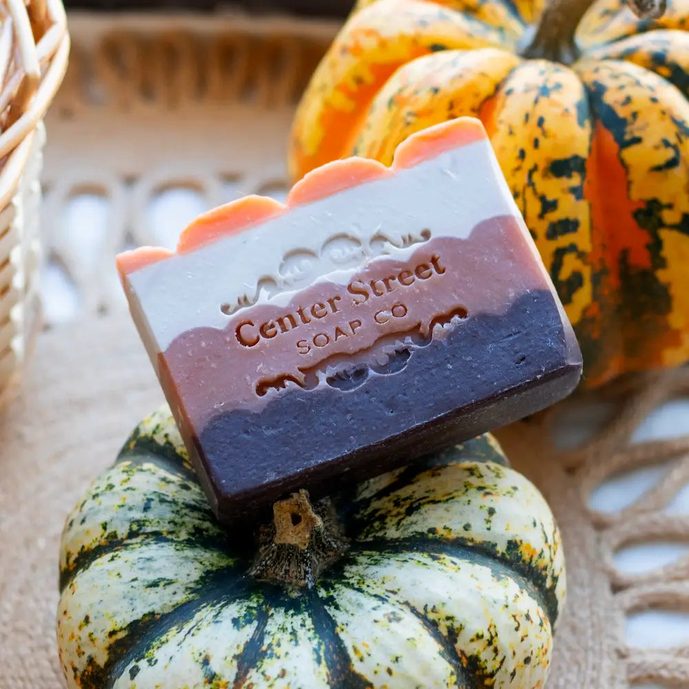 Bar of soap with 'Center Street Soap Co' branding on a pumpkin, with a wicker basket in the background.