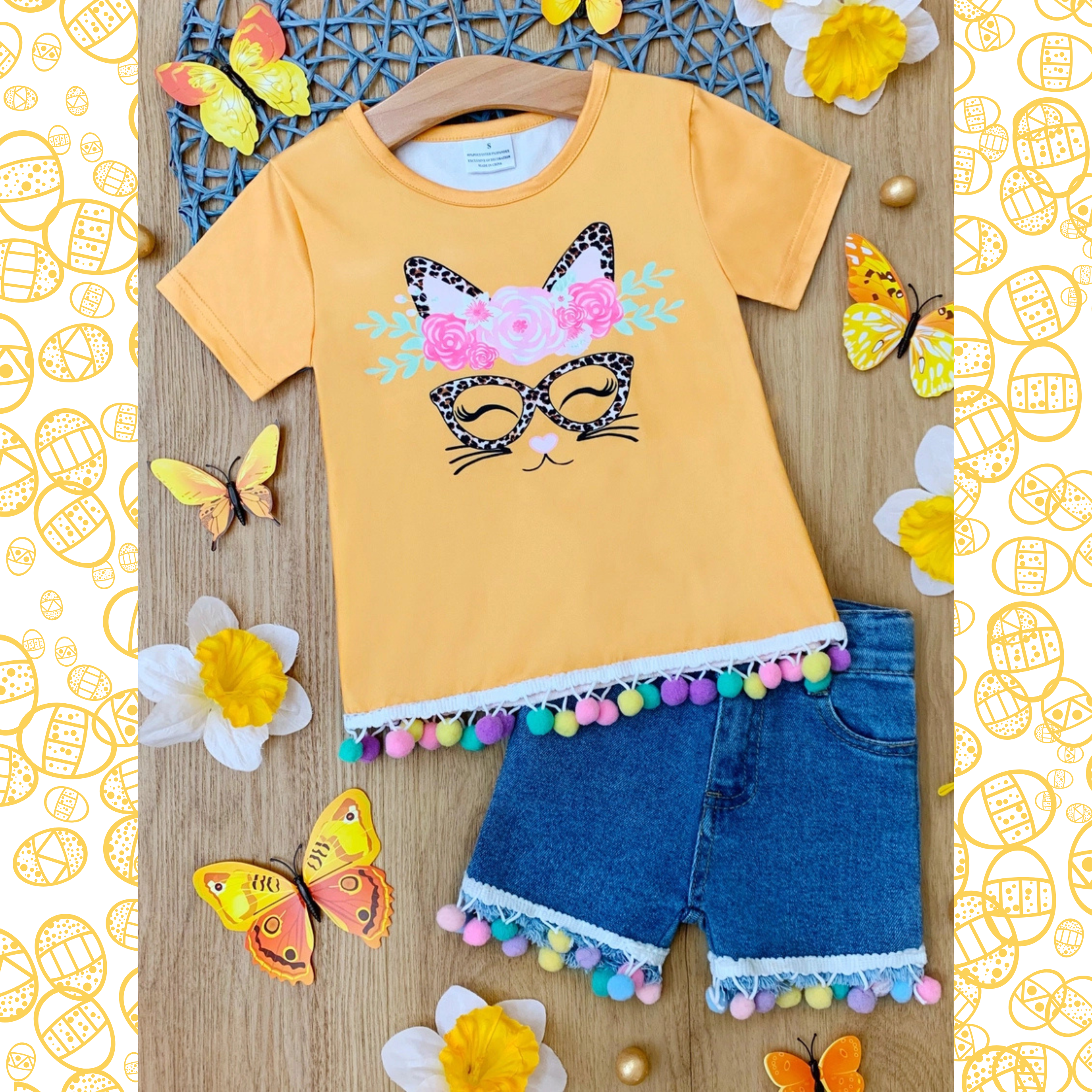 Yellow t-shirt with cat design and denim shorts on a wooden surface with decorative elements.
