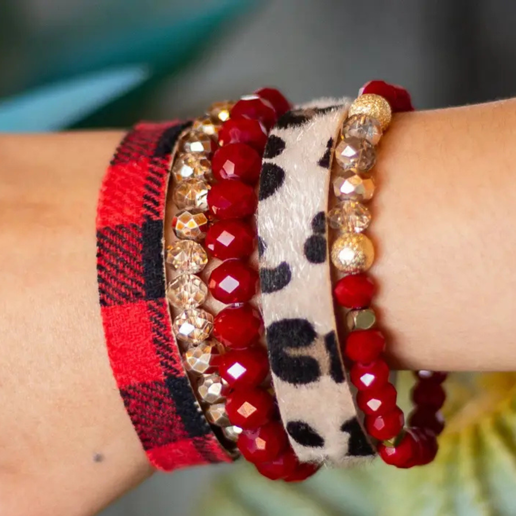 Close-up of a wrist wearing multiple bracelets with red and gold beads, plaid pattern, and leopard print.