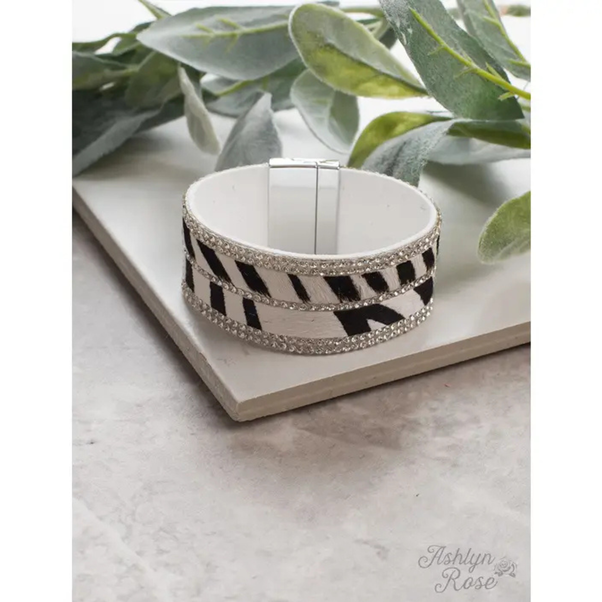 Black and white checkered bracelet with rhinestones on a white surface with green leaves in the background