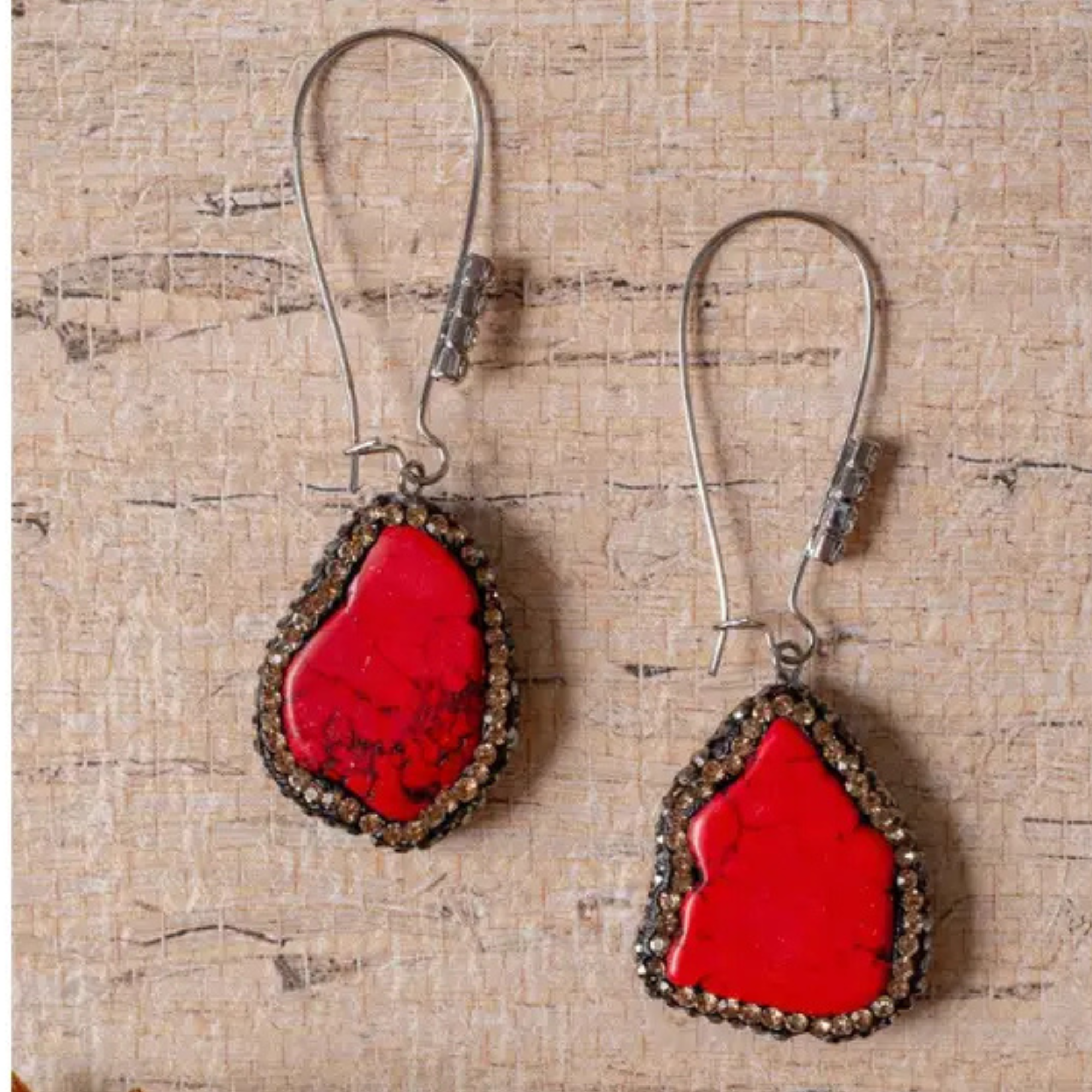 Red teardrop earrings with silver hooks on a textured beige background