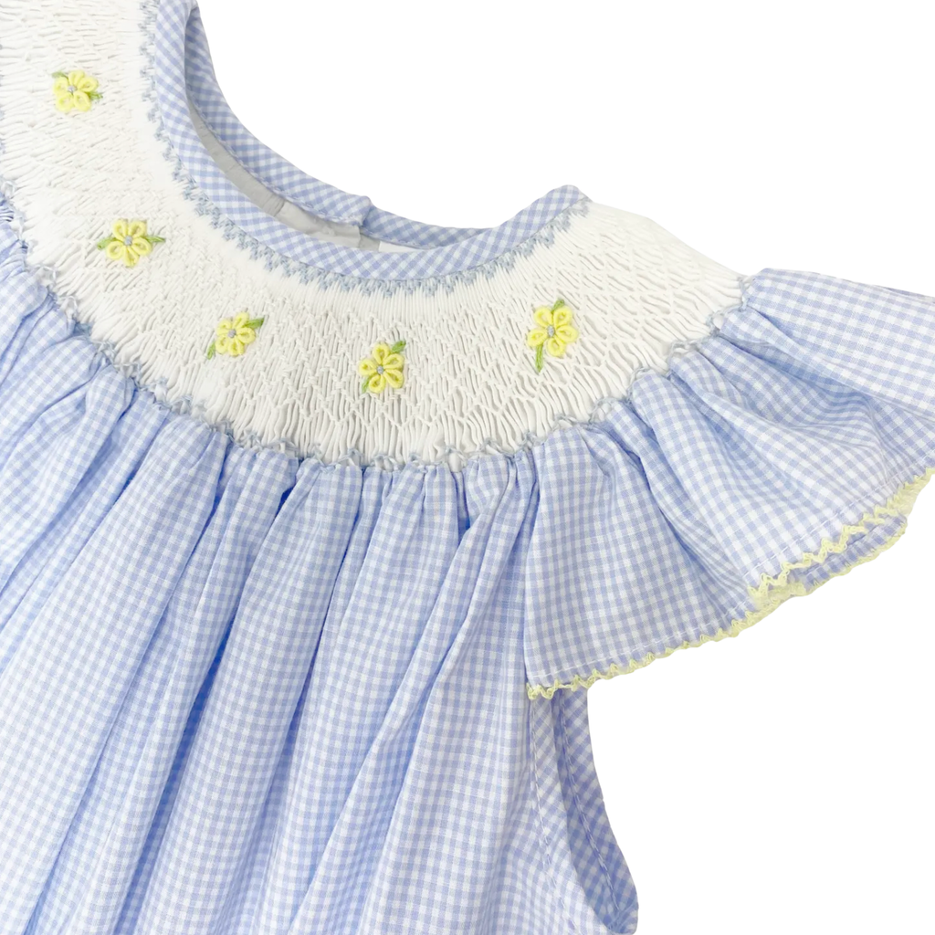 Close-up of a blue checkered dress with white ruffled collar and yellow flower details on a white background.