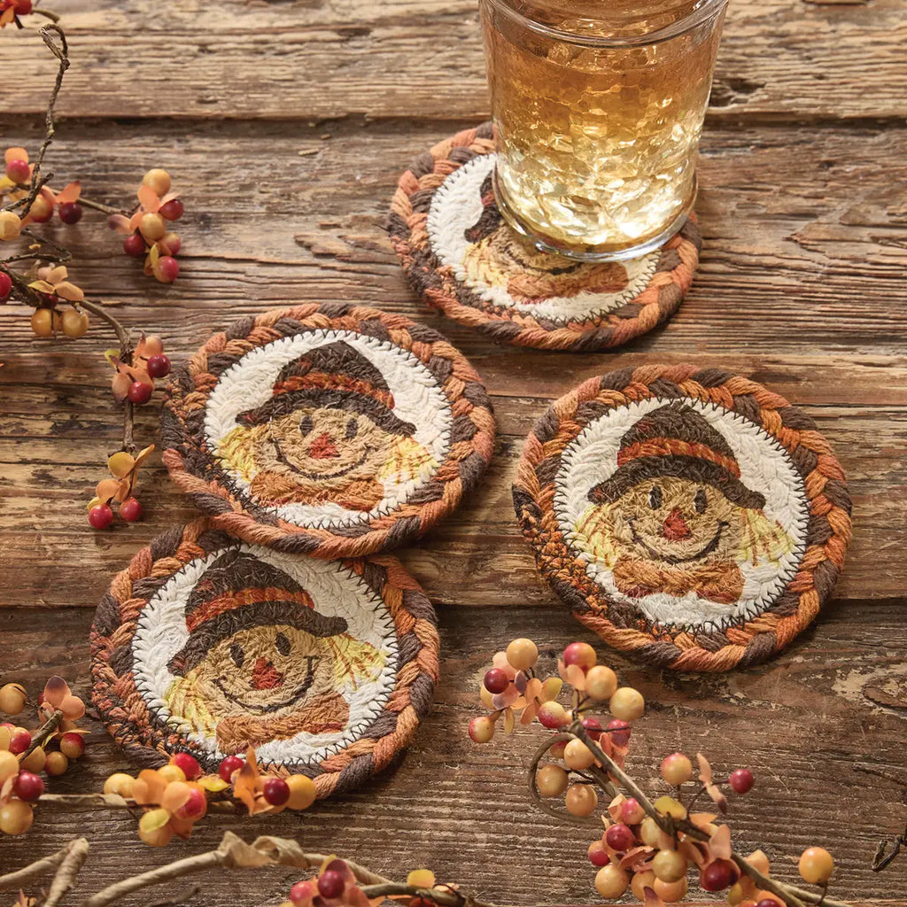 Set of four embroidered coasters with scarecrow designs on a wooden surface with a glass of amber liquid.