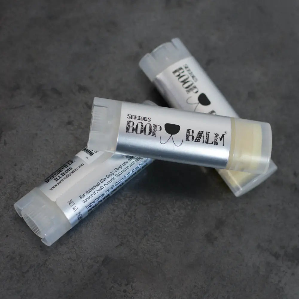 Three lip balms with visible branding on a gray surface