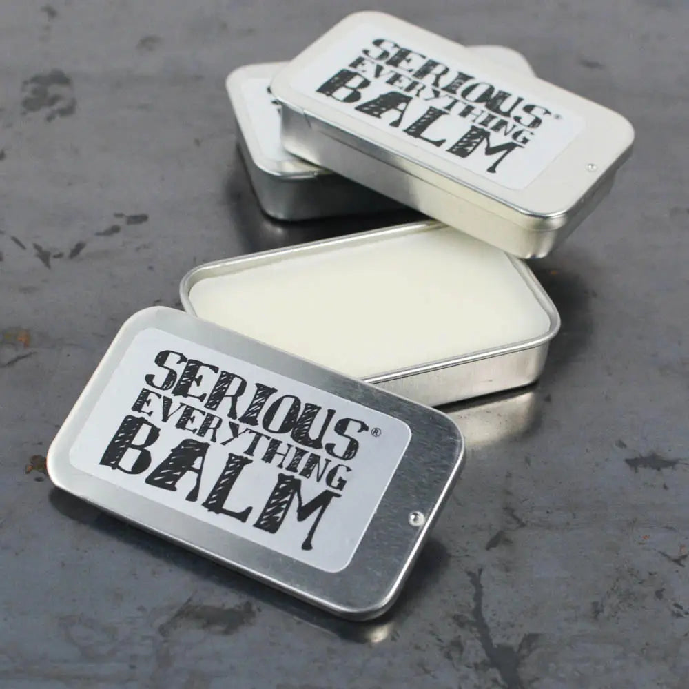 Two open tins of 'Serious Everything Balm' on a textured surface