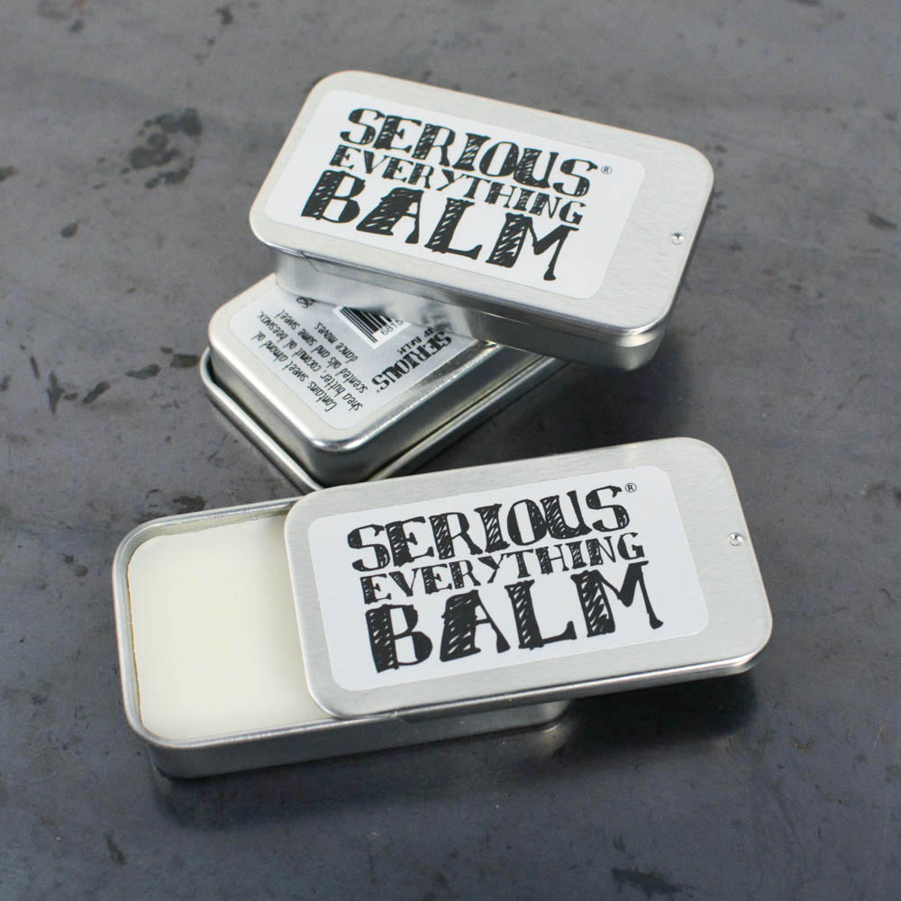Two open tins of 'Serious Everything Balm' on a textured surface
