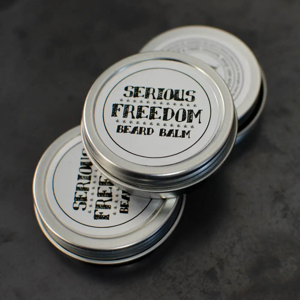 Three tins of 'Serious Freedom Beard Balm' on a dark background