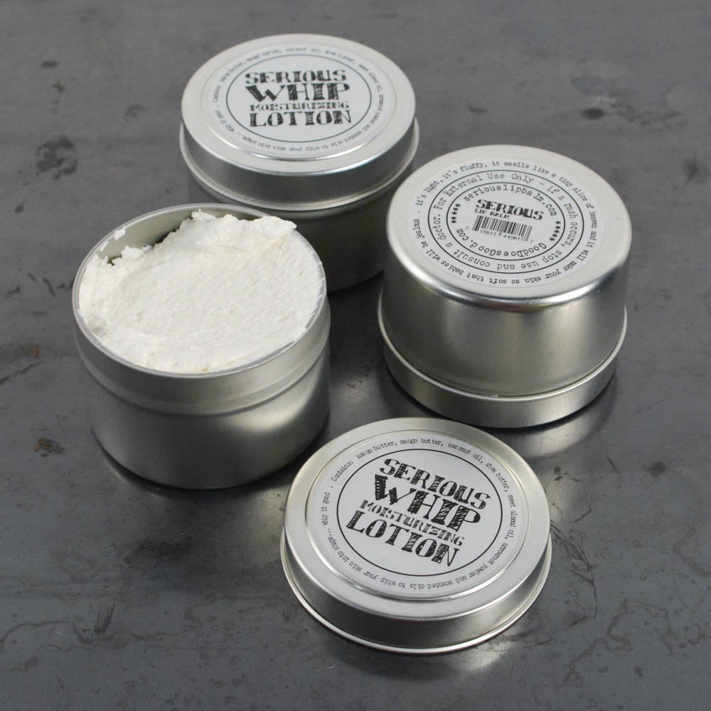 Four tins of 'Serious Whip' moisturizing lotion on a gray surface.