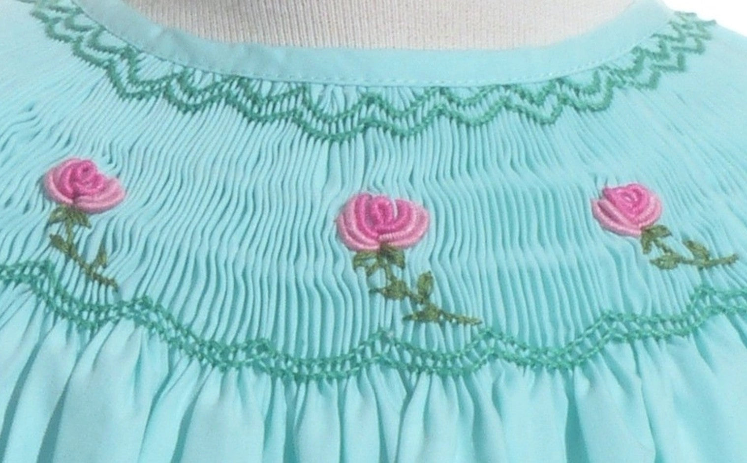 Close-up of a light blue dress with pink rose embroidery on a white background