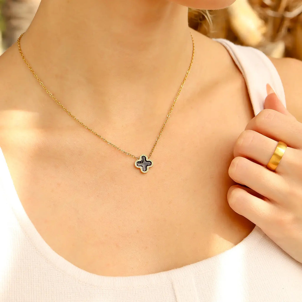 Gold necklace with a clover pendant worn by a person, with a blurred background.