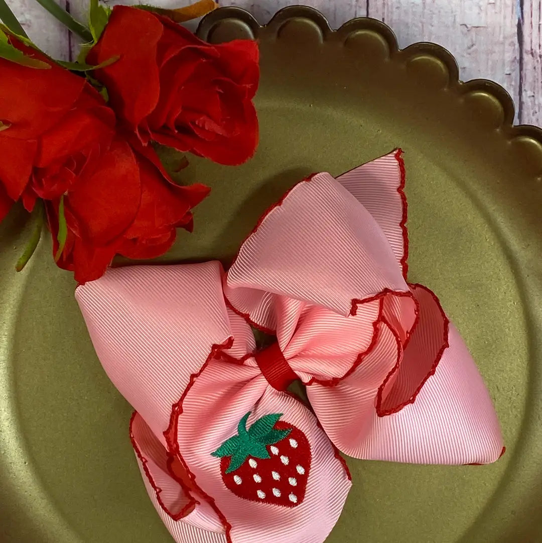 Pink ribbon bow with strawberry design on a gold plate with red roses.