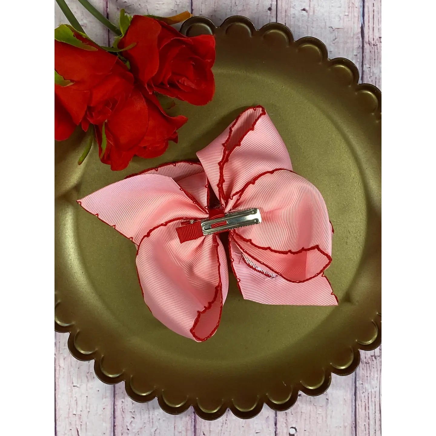 Pink bow hair clip on a green plate with red flowers