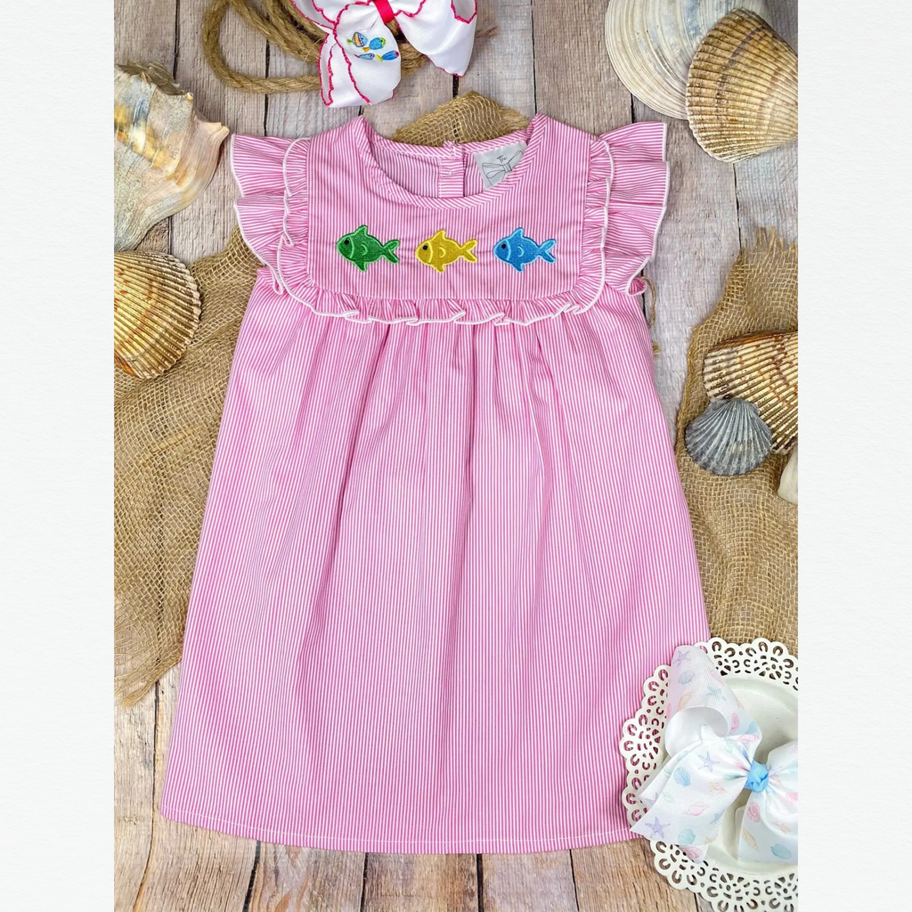 Pink dress with fish embroidery on a wooden surface with seashells