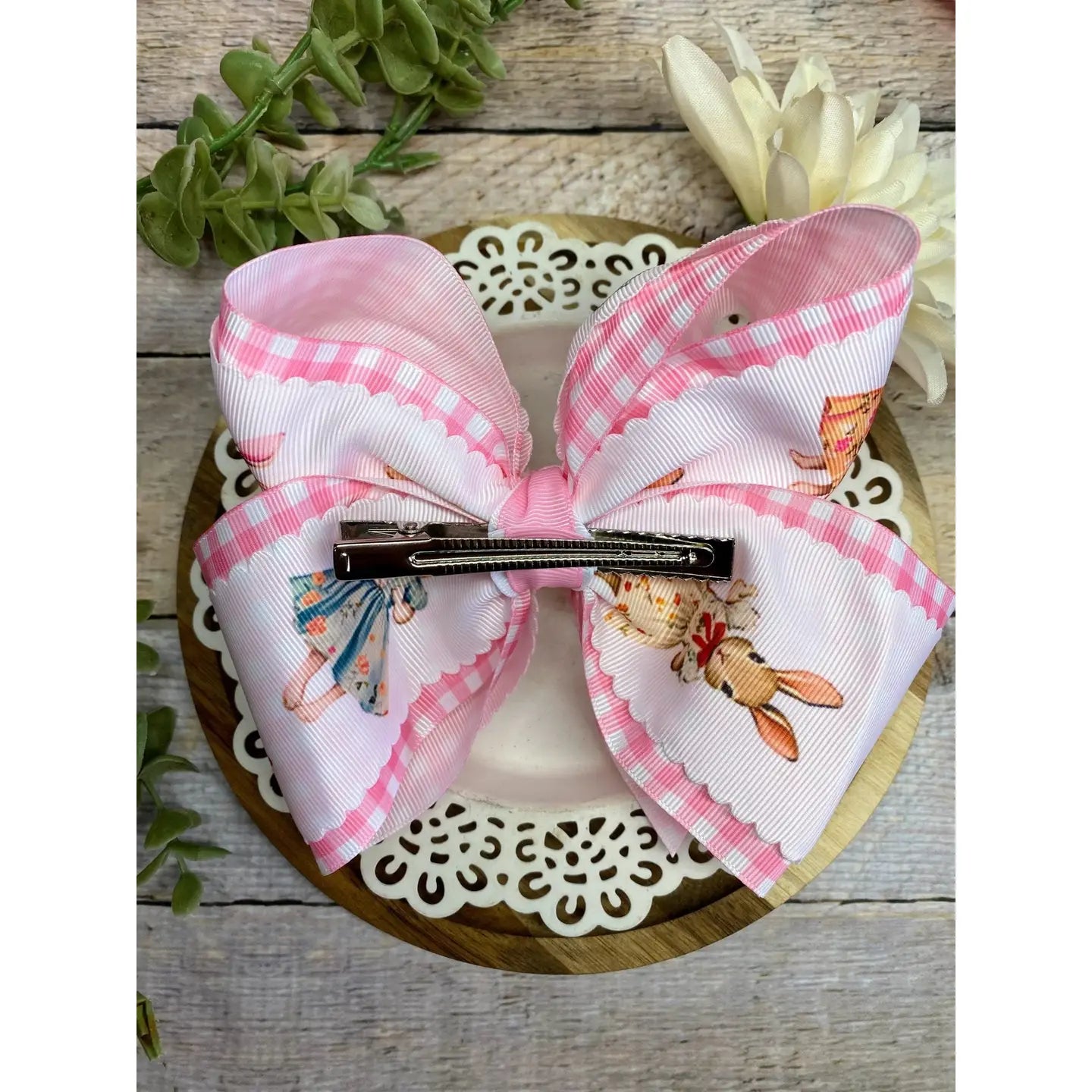 Pink and white checkered bow with cartoon characters on a wooden surface.