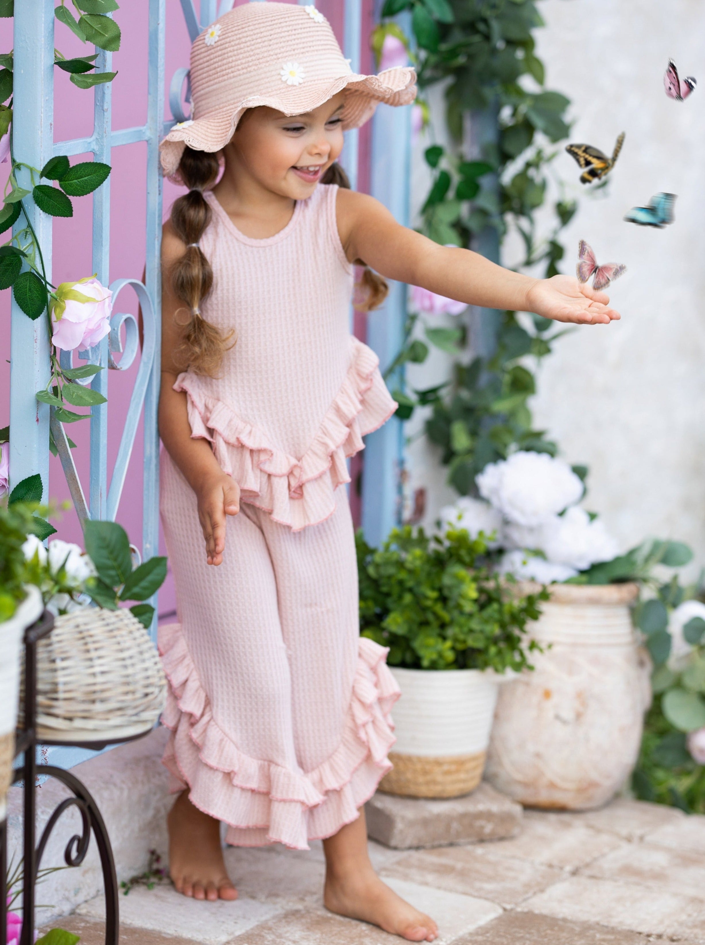 Young girl in a pink dress and hat standing in a garden with butterflies.