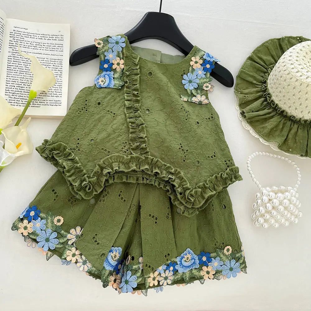 Green children's outfit with floral embroidery on a white surface with flowers and a book.