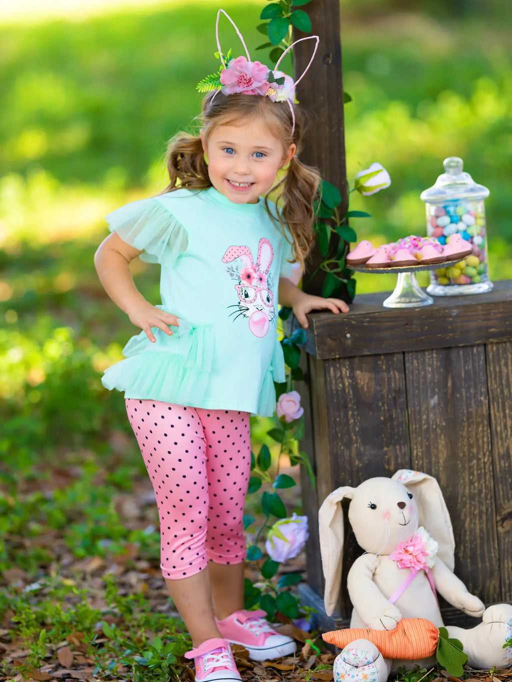 Young girl in Easter outfit with bunny ears and rabbit design, standing outdoors.
