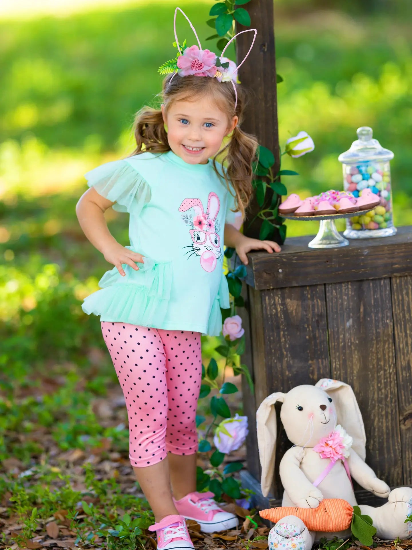 Young girl in Easter outfit with bunny ears and rabbit design, standing outdoors.