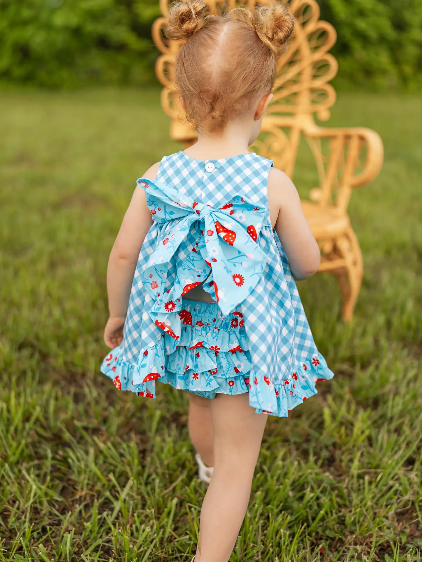 Child wearing a colorful dress with ruffles and a bow, standing in a grassy area.