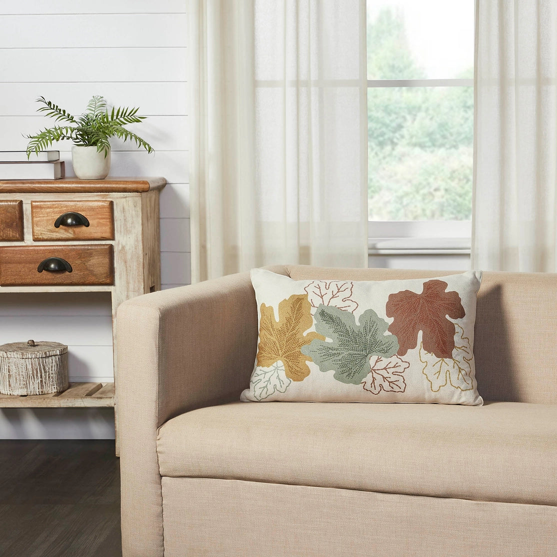 Decorative pillow with leaf patterns on a beige sofa in a room with a wooden side table and plant.