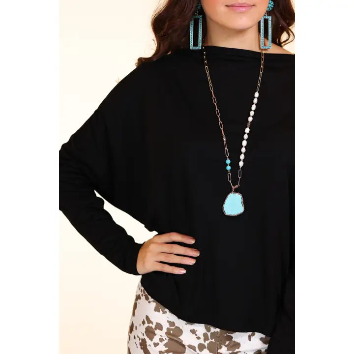 Person wearing a black top with a long necklace featuring a turquoise pendant.
